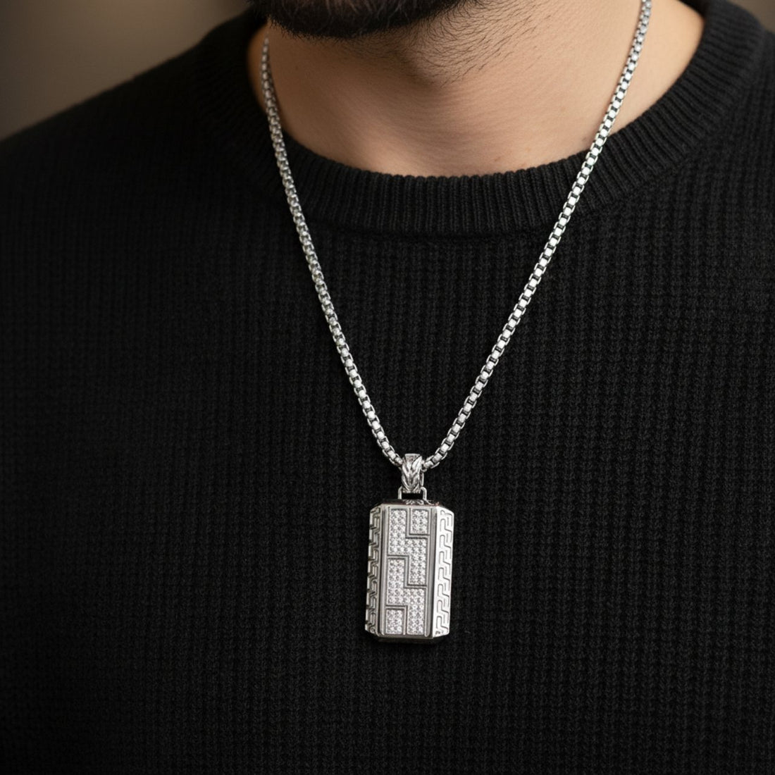 Un colier modern pentru bărbați, cu un lanț din oțel inoxidabil de tip box chain, lung de 60 cm, și un medalion rectangular masiv (4x2 cm). Medalionul este decorat cu cristale de zirconiu dispuse într-un model geometric, adăugând strălucire.